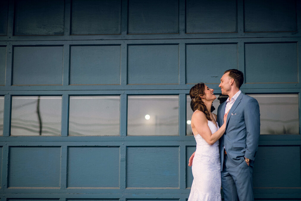 A bride and groom embracing in front of a garage door.