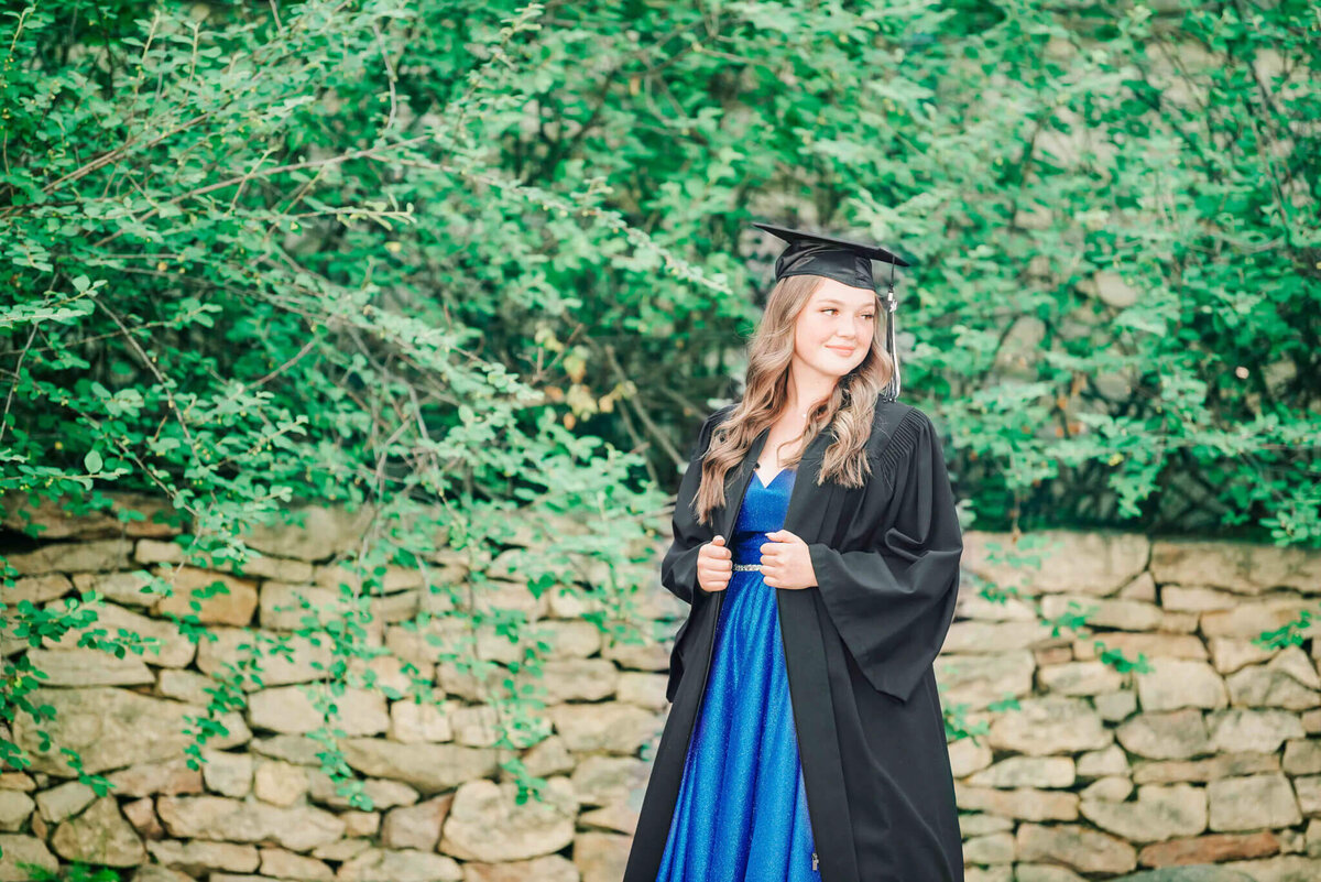 In a hidden alcove a girl wears her grad dress and grad cap looking over her shoulder. 