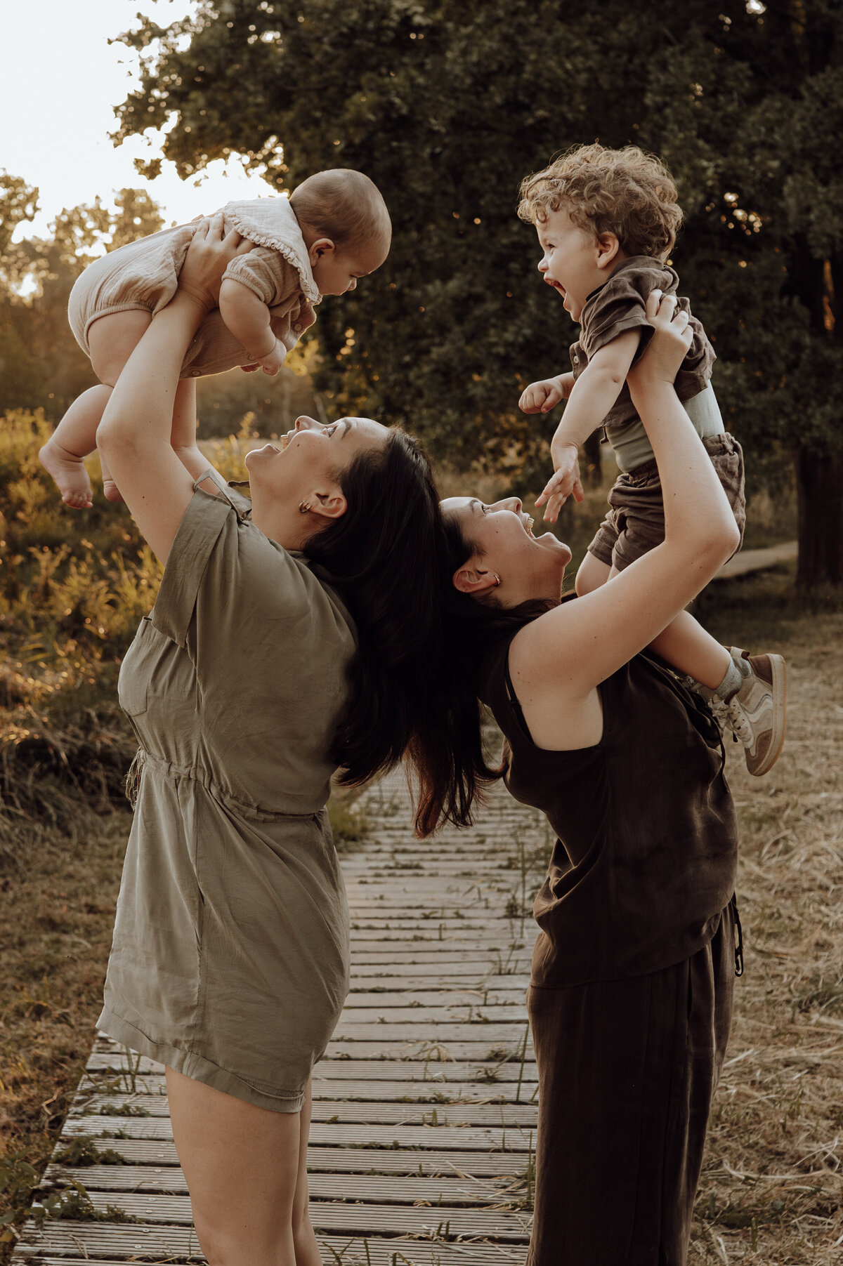 Twee mama's met kindjes spelen tijdens gezinsshoot in het bos