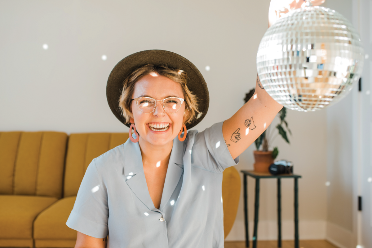 Philadelphia photographer Heather McBride in a brown hat and gray shirt holding a shimmering disco ball.
