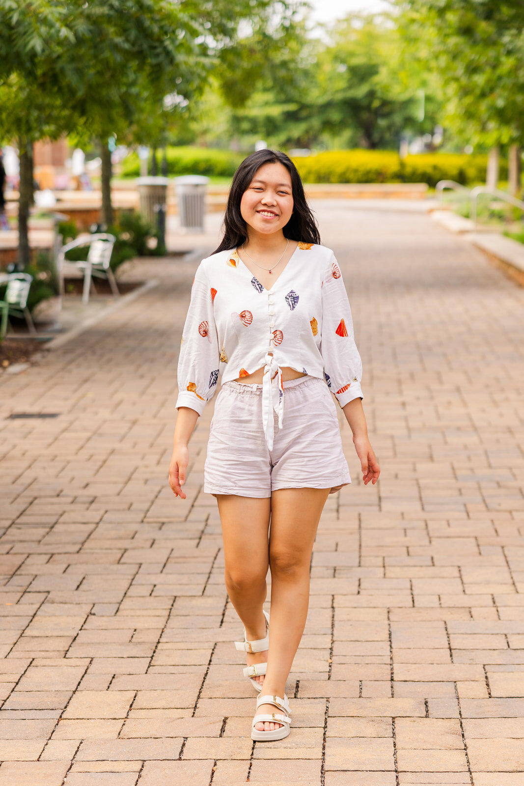 senior girl walking towards the camera in a urban street in Sandy Spring wearing a white short and a white blouse with patterns