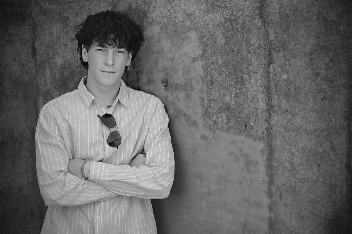 Relaxed senior portrait with sunglasses, styled in cream jeans and retro layers, photographed in Charlotte’s industrial district.
