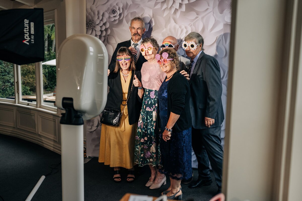 a group of adults pose in front of a white photo booth at pemberton