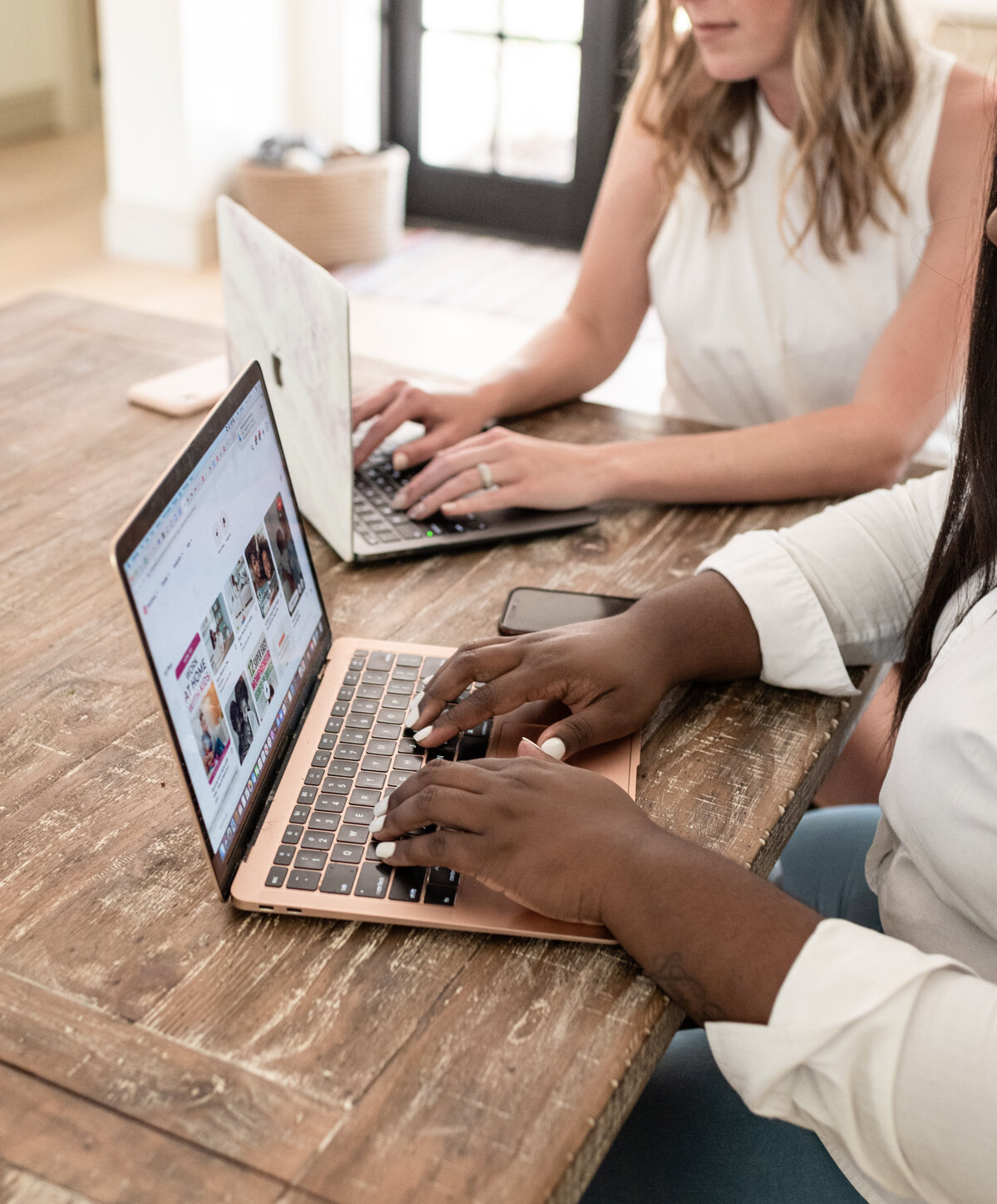 two women are working on their macbooks at the table