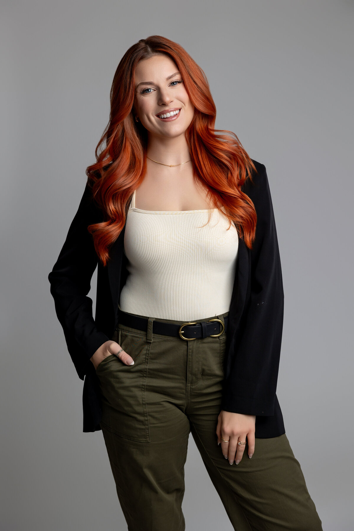 Red-haired woman in black blazer smiling confidently in studio portrait. Photograph by Yucaipa branding photographer Kaitlyn Dawn Photography.