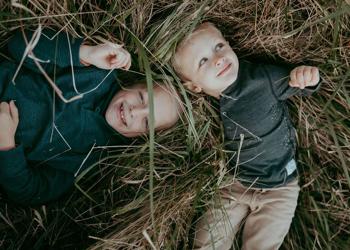 Two brothers lay in tall autumn grasses together during a family photo session.