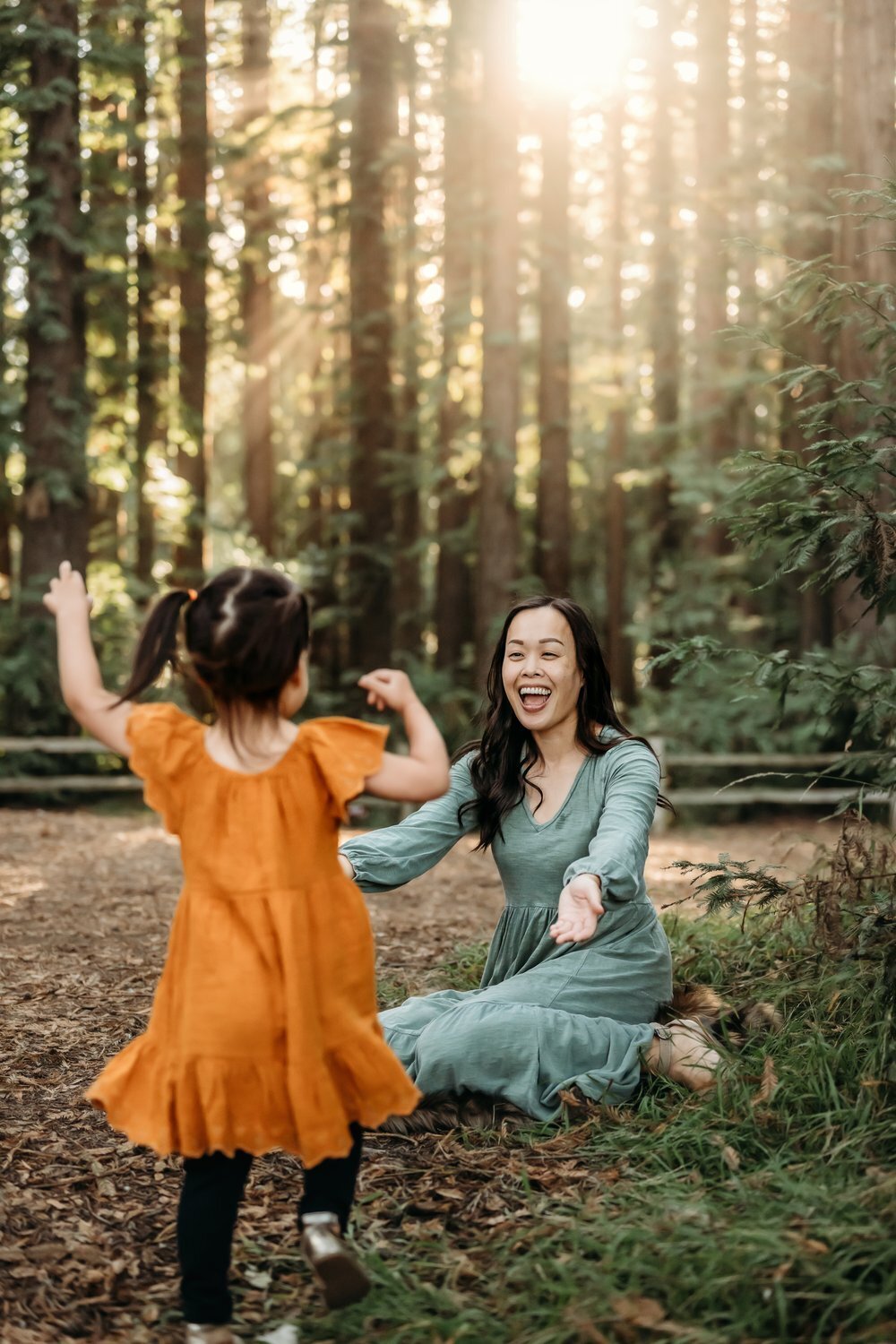 toddler in yellow dress runs toward a happy mom in the redwood forest