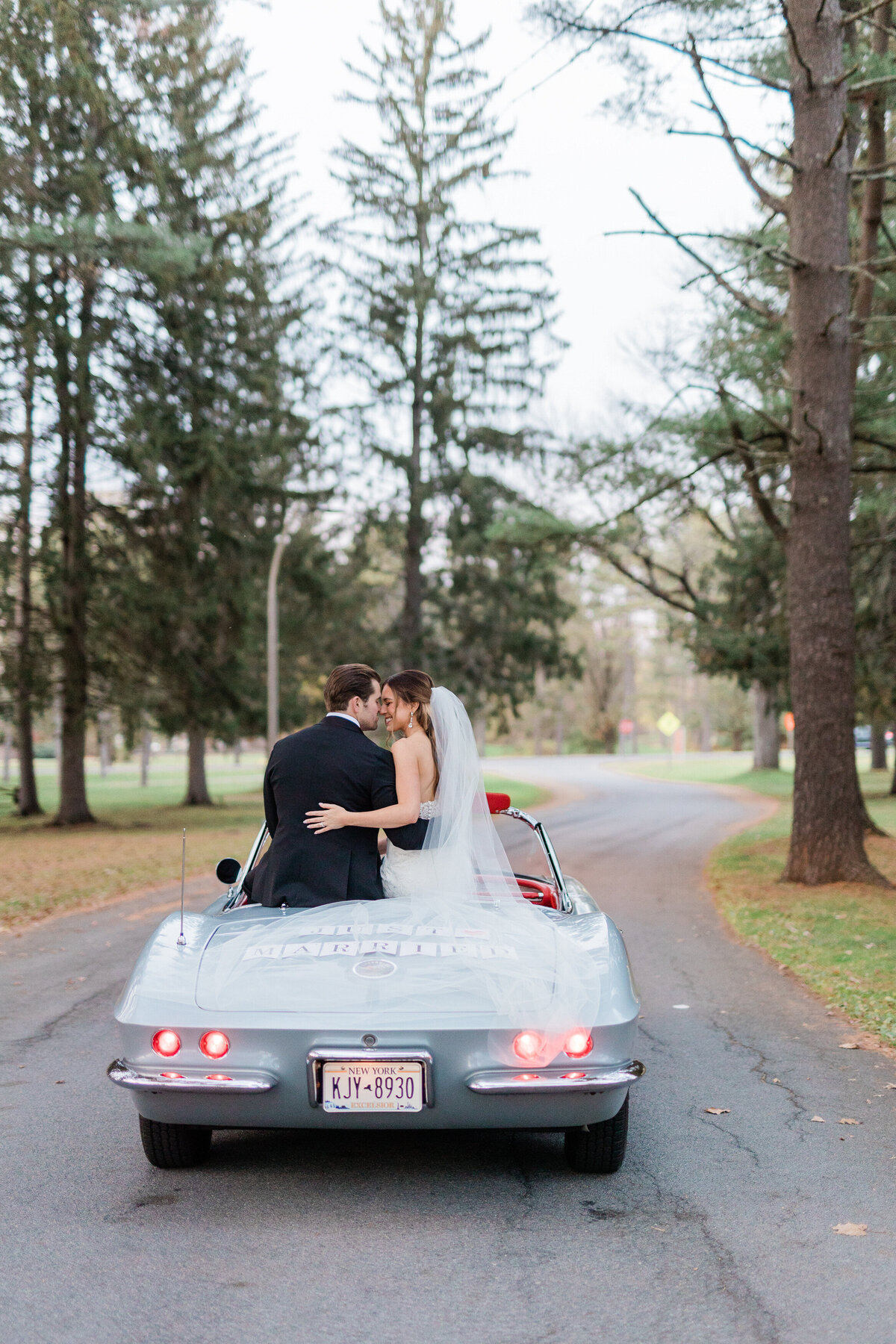 Newlyweds sit on the top of their white convertible 