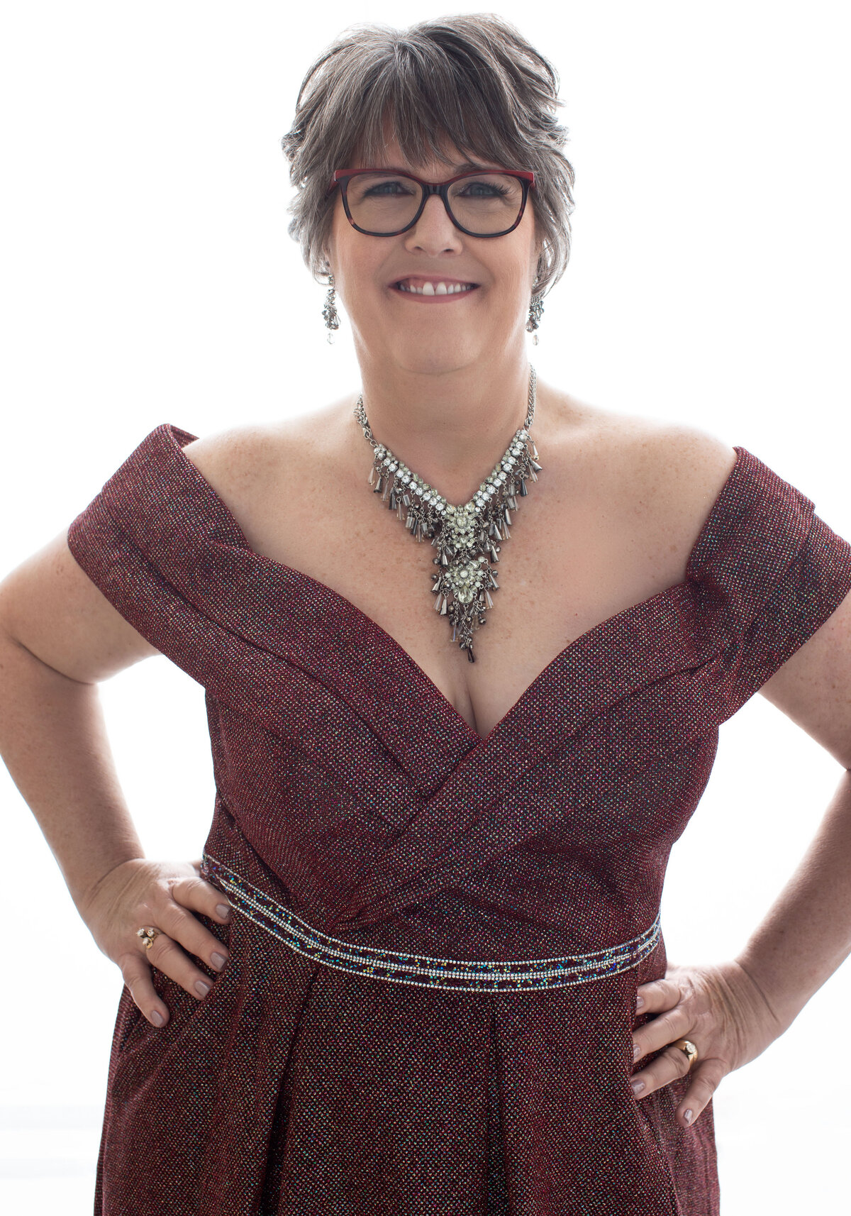 Cincinnati portrait featuring a joyful woman adorned in a detailed necklace, wearing glasses, and elegantly styled in an off-shoulder patterned dress. The image exemplifies confident and radiant studio photography.