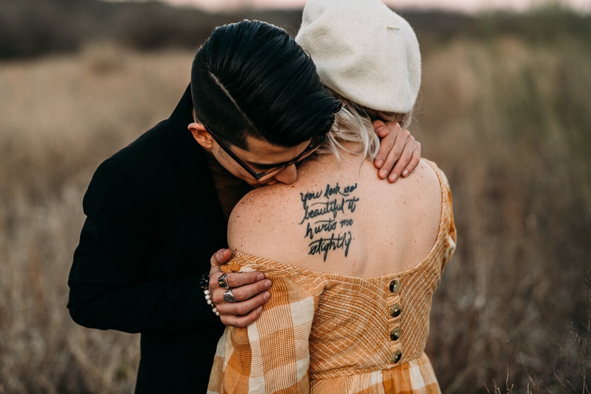 Couples Photography, Man in a suit holds and kisses the shoulders of a girl in a  with a tattoo