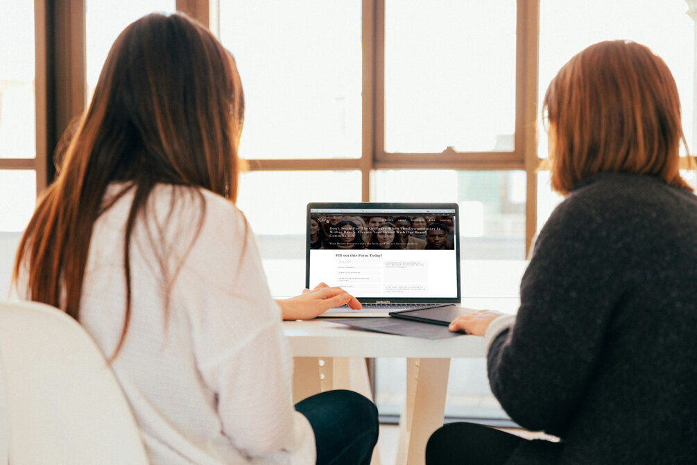 two women sitting on a desk reviewing website designed by ATamez Design