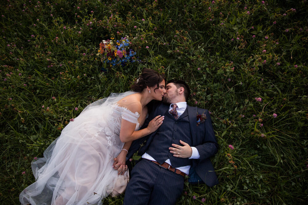 married couple lays in a field of wildflowers and kisses