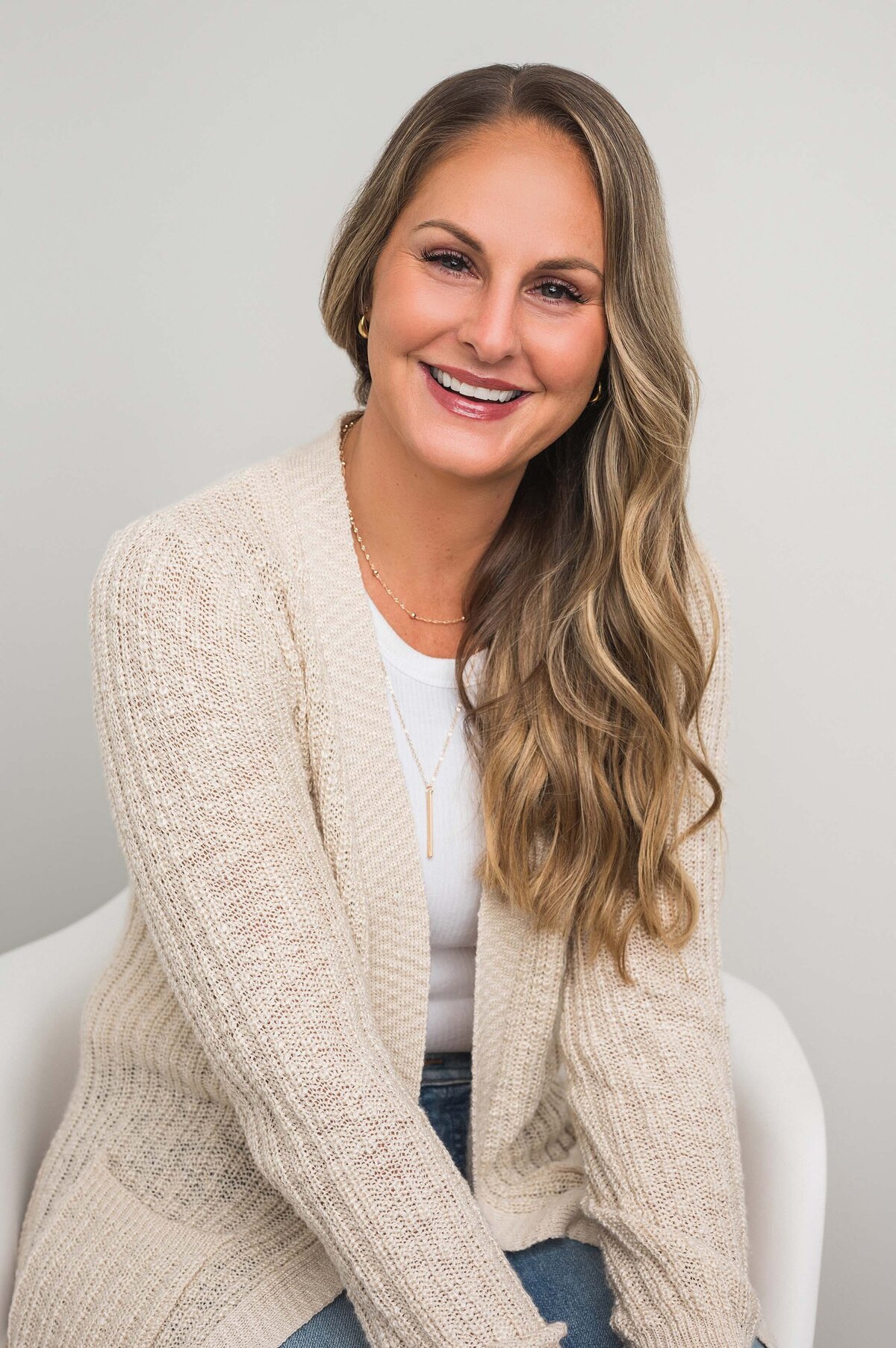 Smiling woman in a beige cardigan, sitting comfortably with a white top