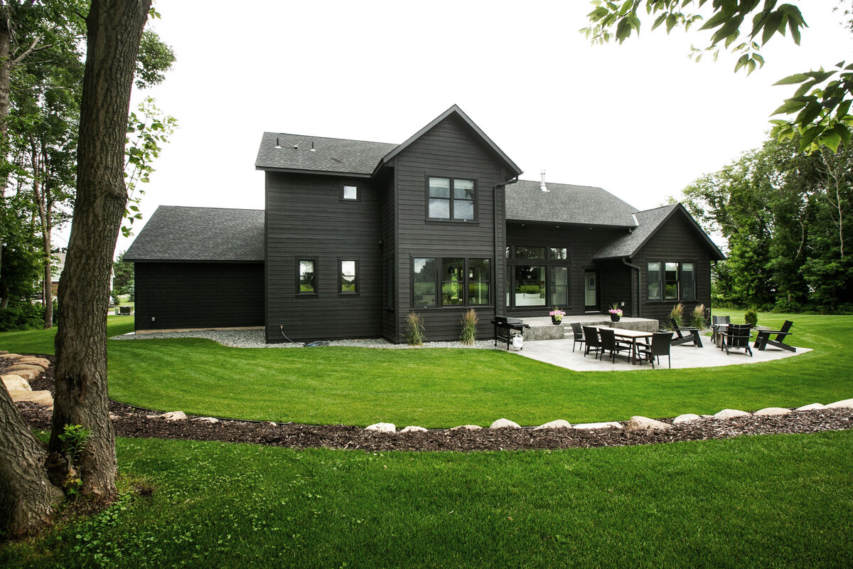 Exterior view of custom home in Otsego, Minnesota with black siding, large patio and windows built by Cornerstone Custom Builds