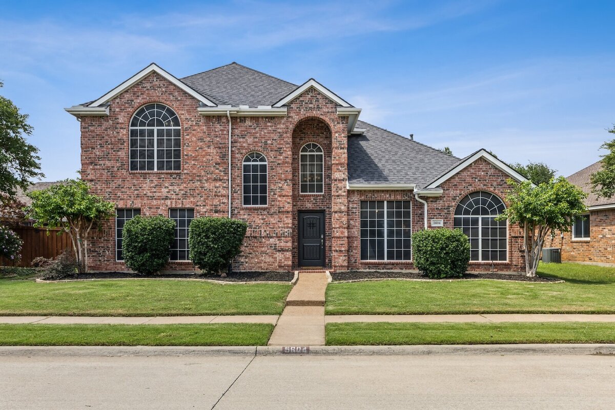 Front exterior 5604 Glenview Lane in The Colony, Texas — a two-story brick home with mature trees, and charming curb appeal, listed by Haven Realty Group.