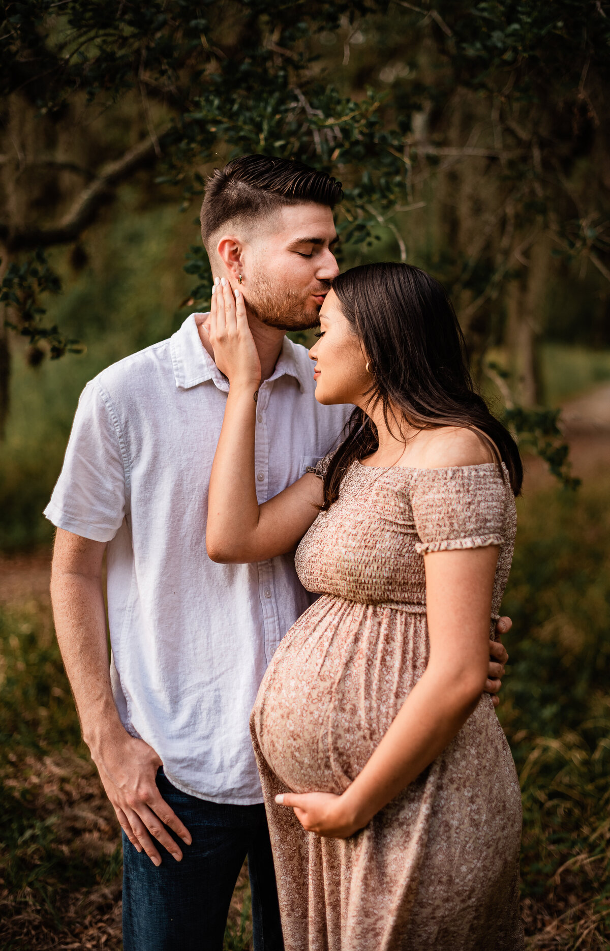 A Houston area expectant mom holds her belly and pulls her boyfriend toward her face as he kisses her forehead.