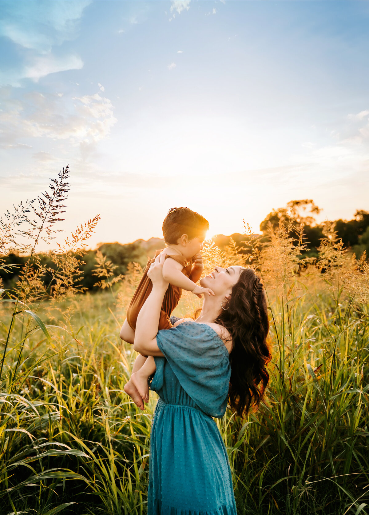 Family Photographer, a mother holds her baby in the air in a field of tall grass