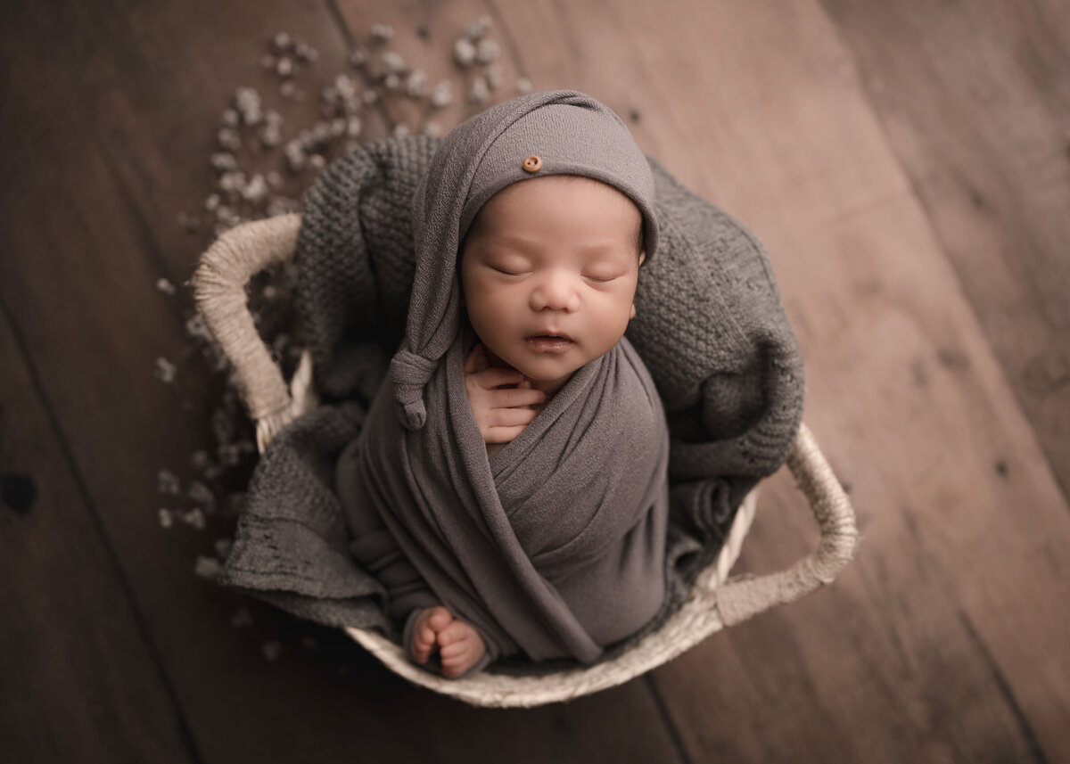 Aerial image of baby boy at his Temecula newborn photoshoot. Baby is wrapped in grey with his toes and fingers peeking out of the swaddle. He is wearing a long cap. Captured by best Temecula newborn photographer Bonny Lynn Photography