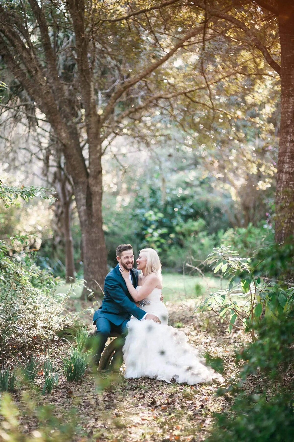 A bride and groom sitting on a bench in a wooded area.