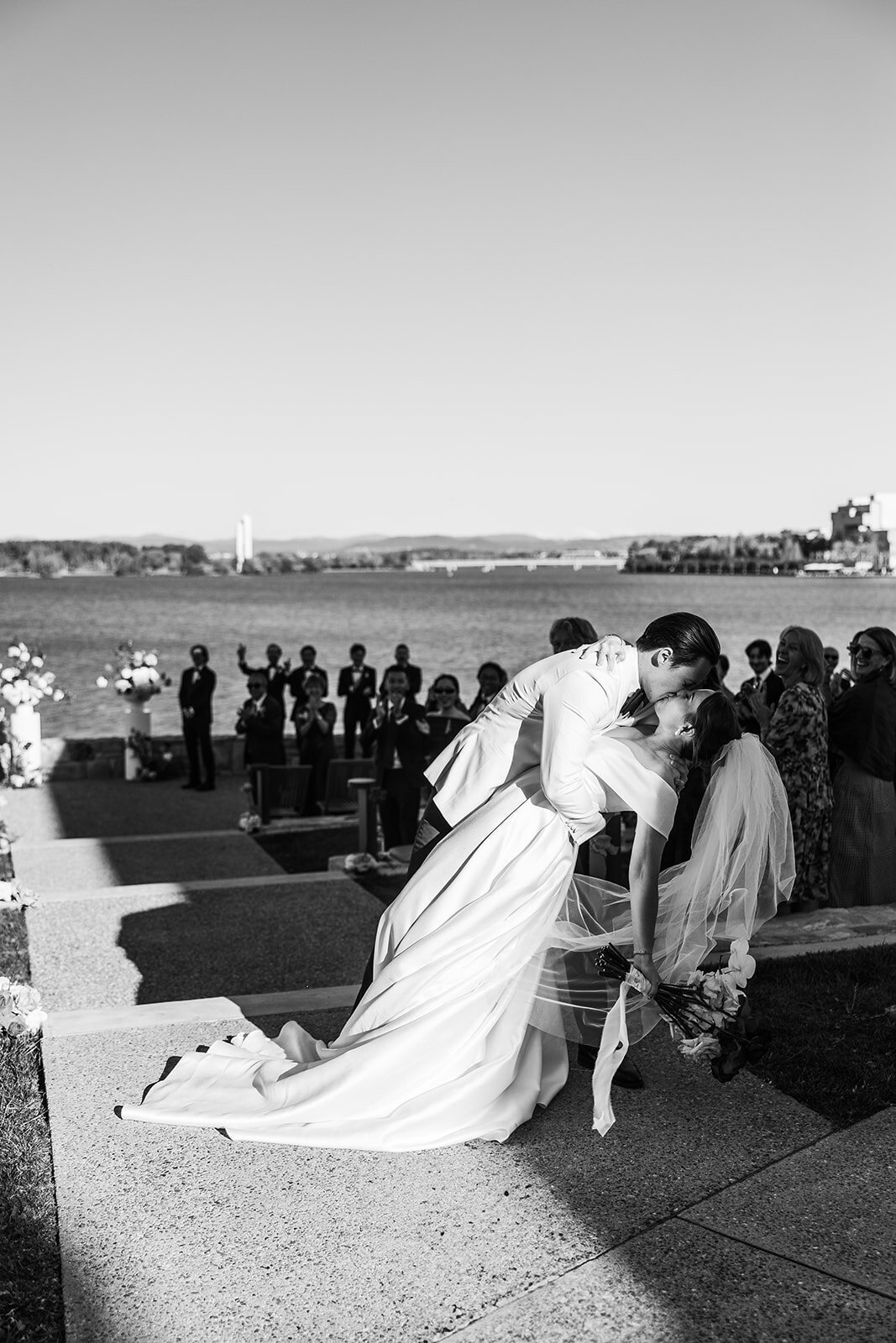 Black and white image of a dip kiss between a bride and groom after walking down the aisle at their wedding.