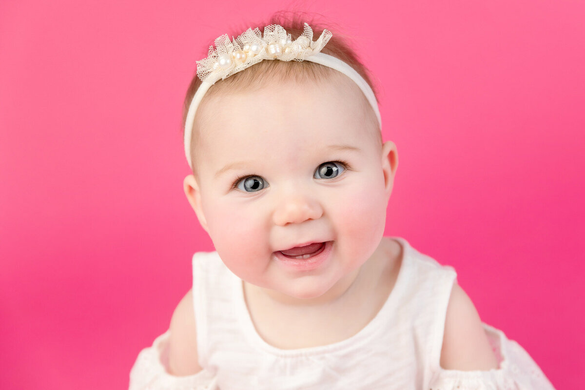 6 month old baby girl smiles in a portrait on a pink background
