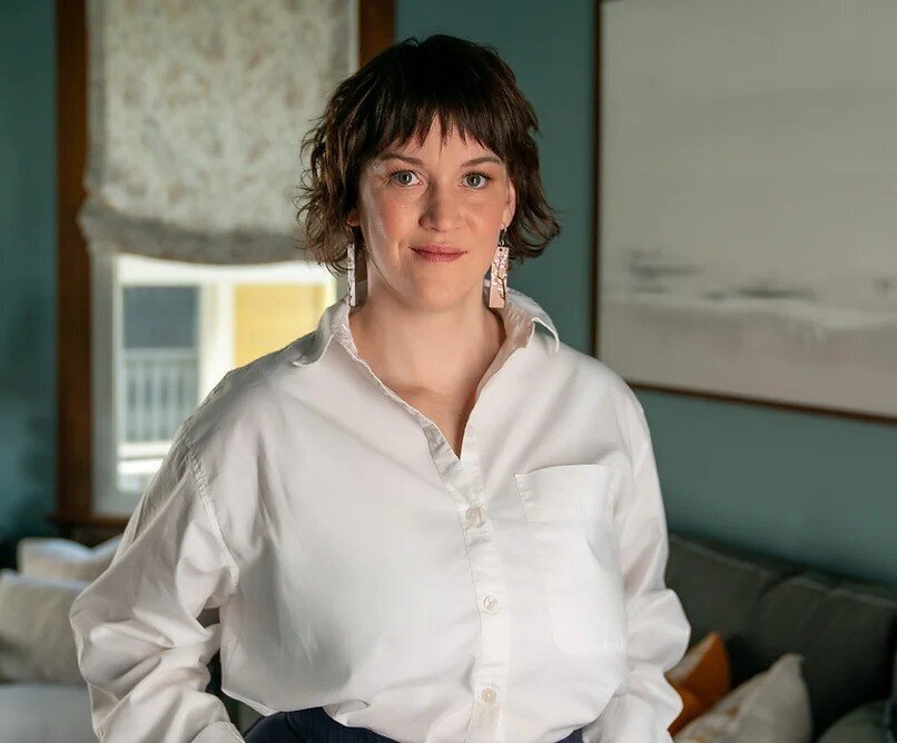 A woman wearing a white button down shirt with short brown hair stands in a living room