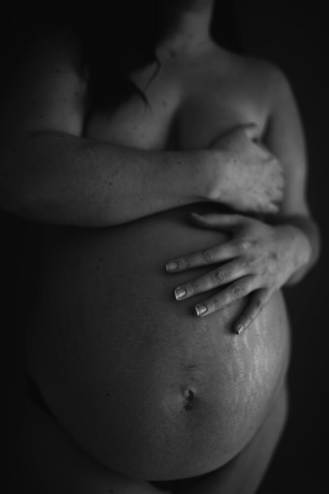Black and white image of women holding her pregnant belly with strethmarks