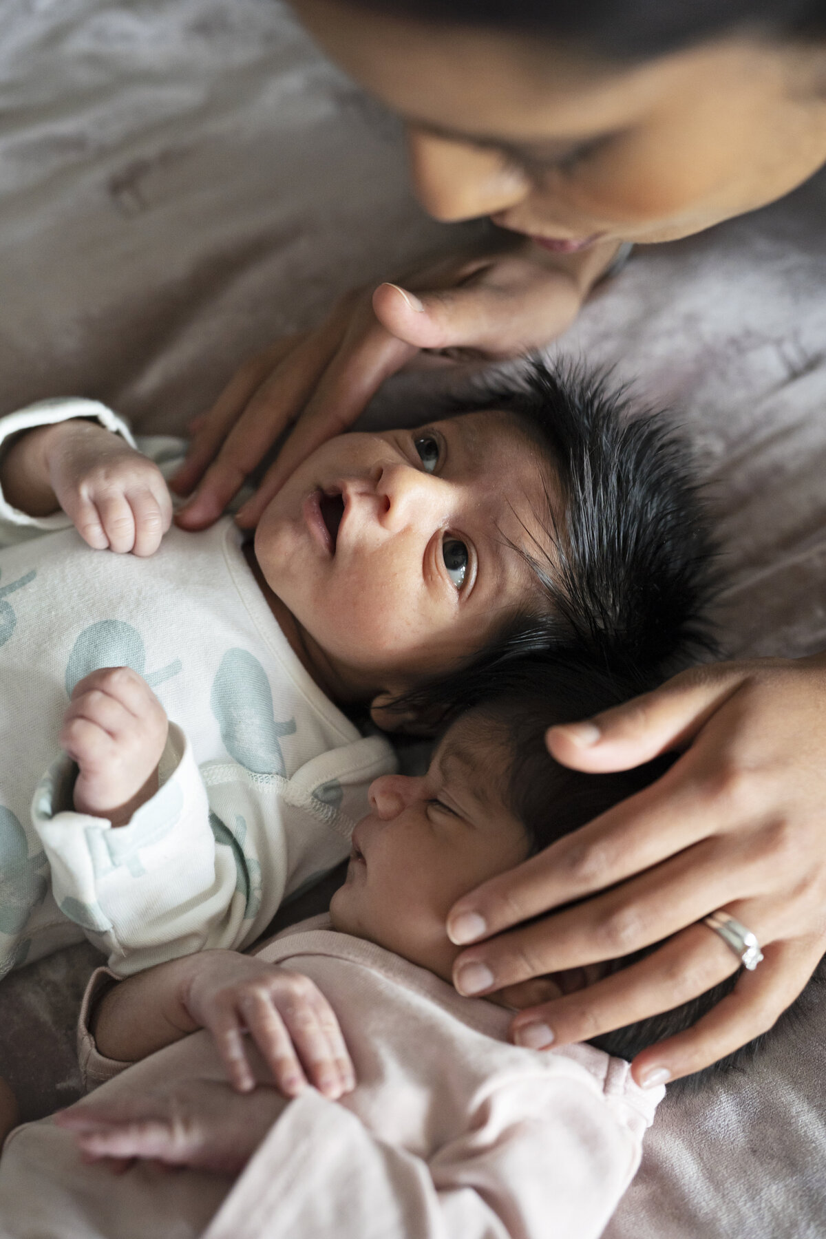 A mother shushes her newborn baby twins to sleep during an at home newborn photo shoot