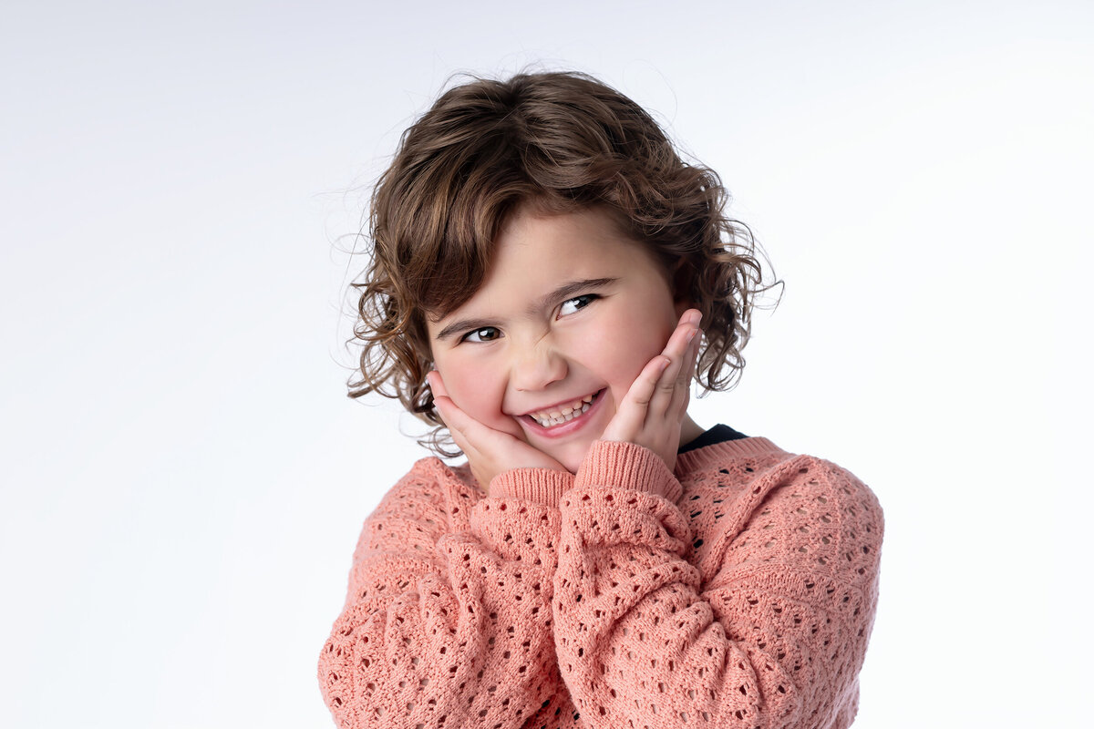 Young girl smiles in a pink sweater as she rests her chin in her hands