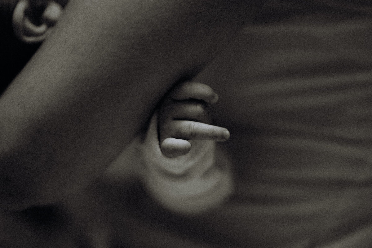 An artistic close-up of a baby’s tiny hand, gently resting against a parent's arm, captured in soft, moody lighting during a lifestyle family session in Fort Worth, Texas.