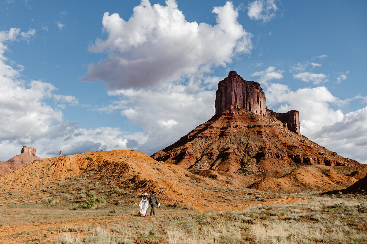 A couple walking to their ceremony spot on the Ida Gulch Trail in Moab. They are both wearing cowboy hats, and they are walking towards some epic red rock formations.