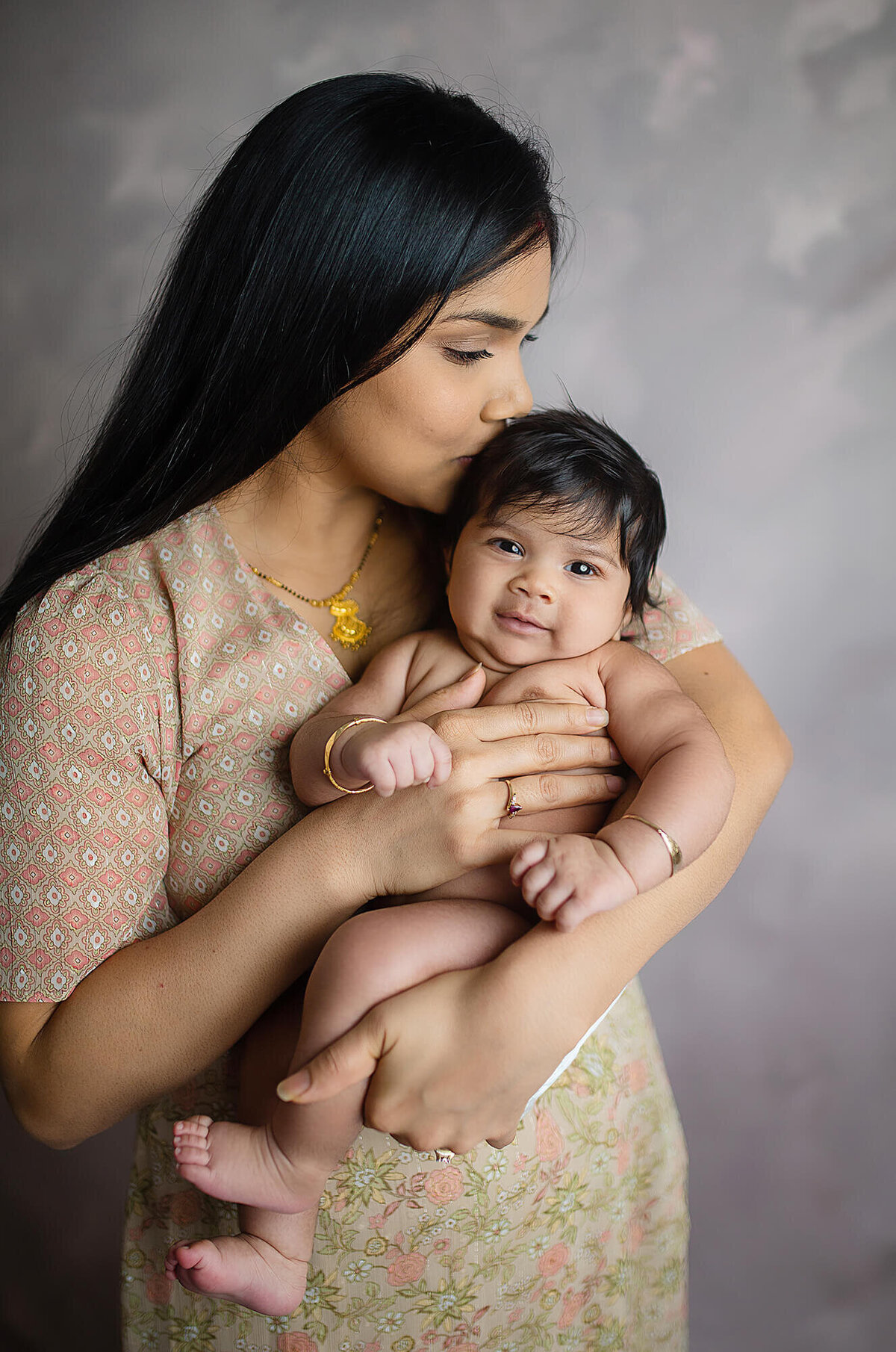 Dark haired mother cuddling and kissing on naked baby smiling 