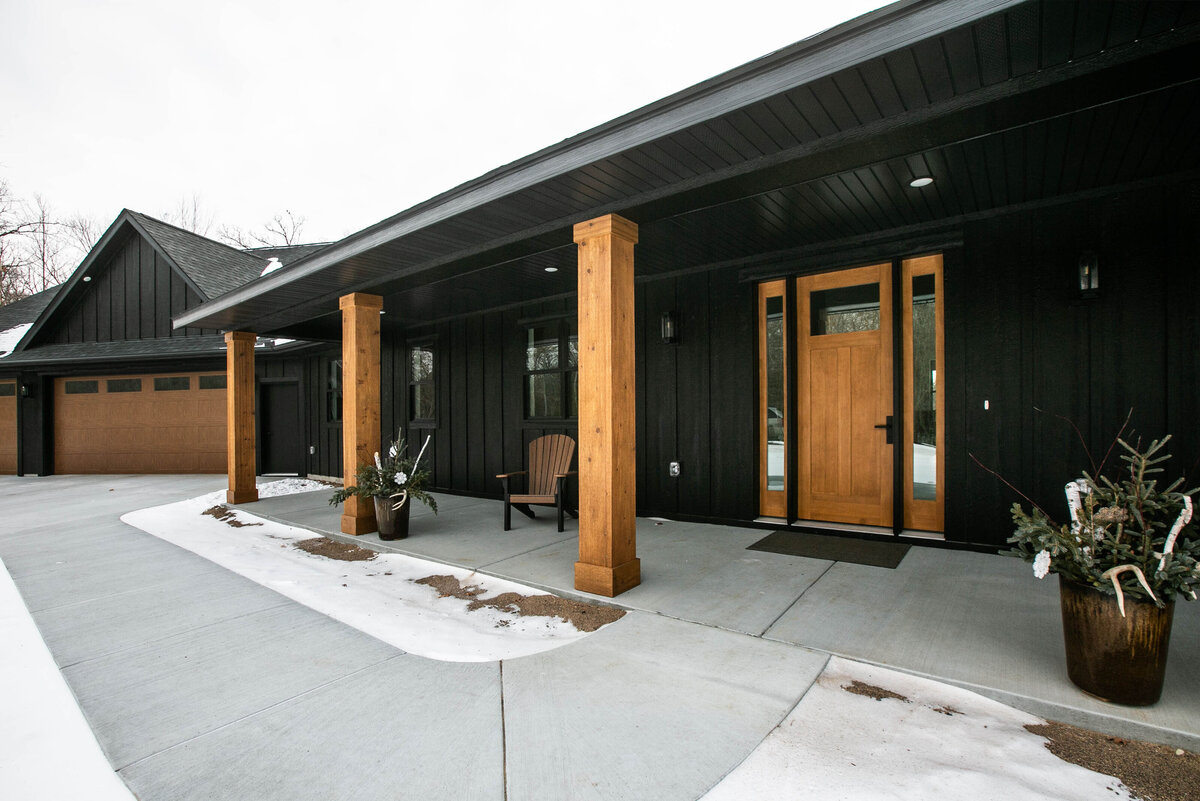 Exterior view of custom home in Elk River, Minnesota with black siding, wood details and front porch built by Cornerstone Custom Builds