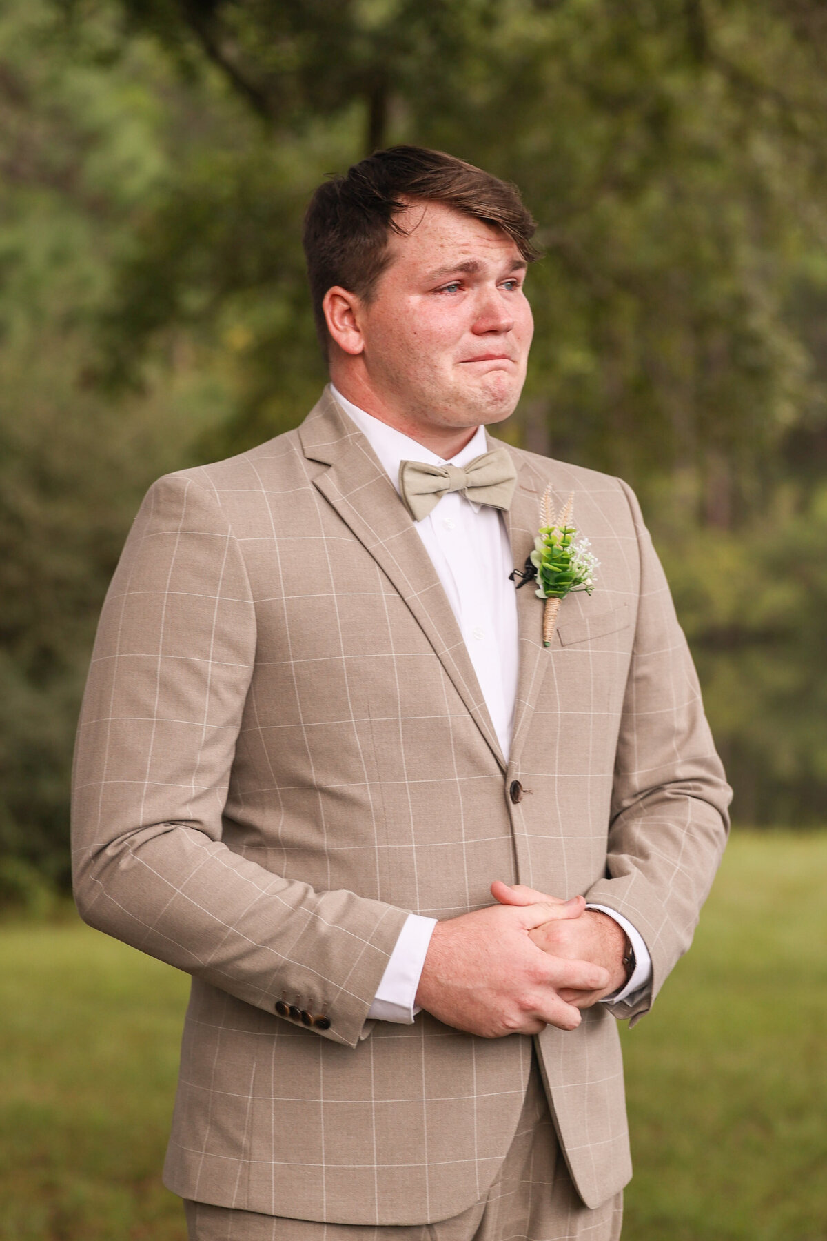 groom crying while bride walks down the aisle wearing tan suit
