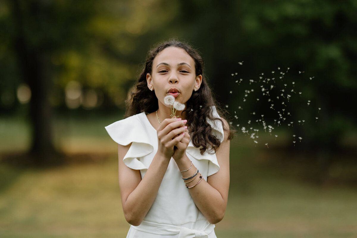 candid portrait Longview, TX of girl in white romper blowing the ligules off of a dandelion