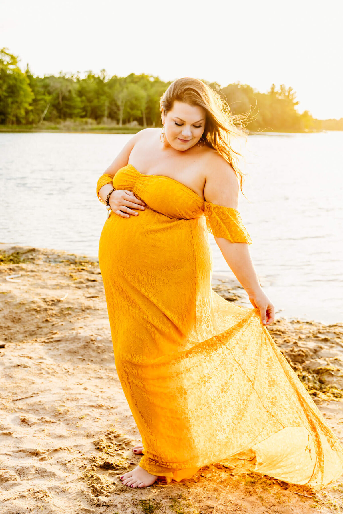 glowing pregnant mom playing with yellow lace dress as she walks on the beach for motherhood photos