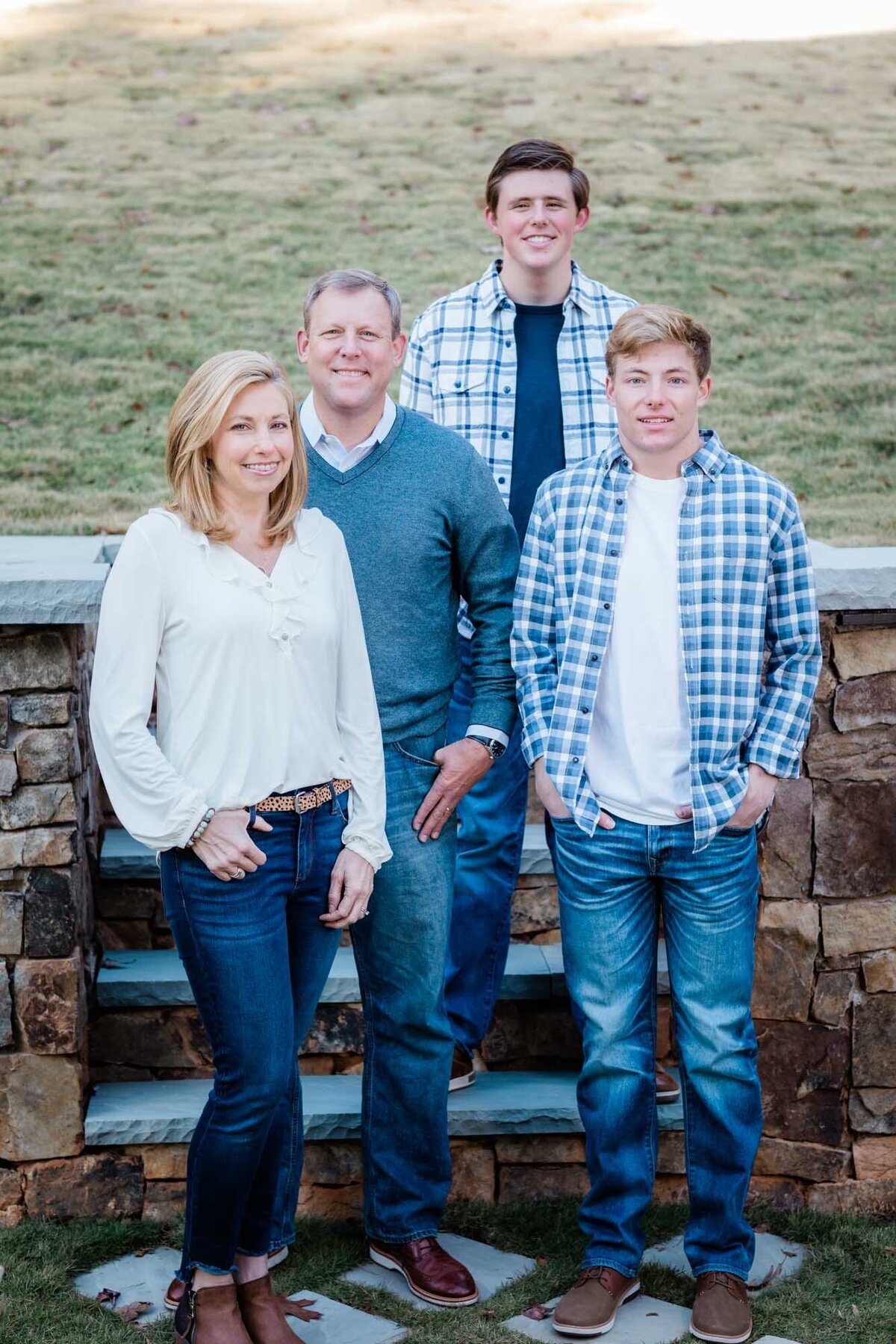 A family portrait of a mother, father and their two sons  dressed in blue standing on stairs in their backyard.