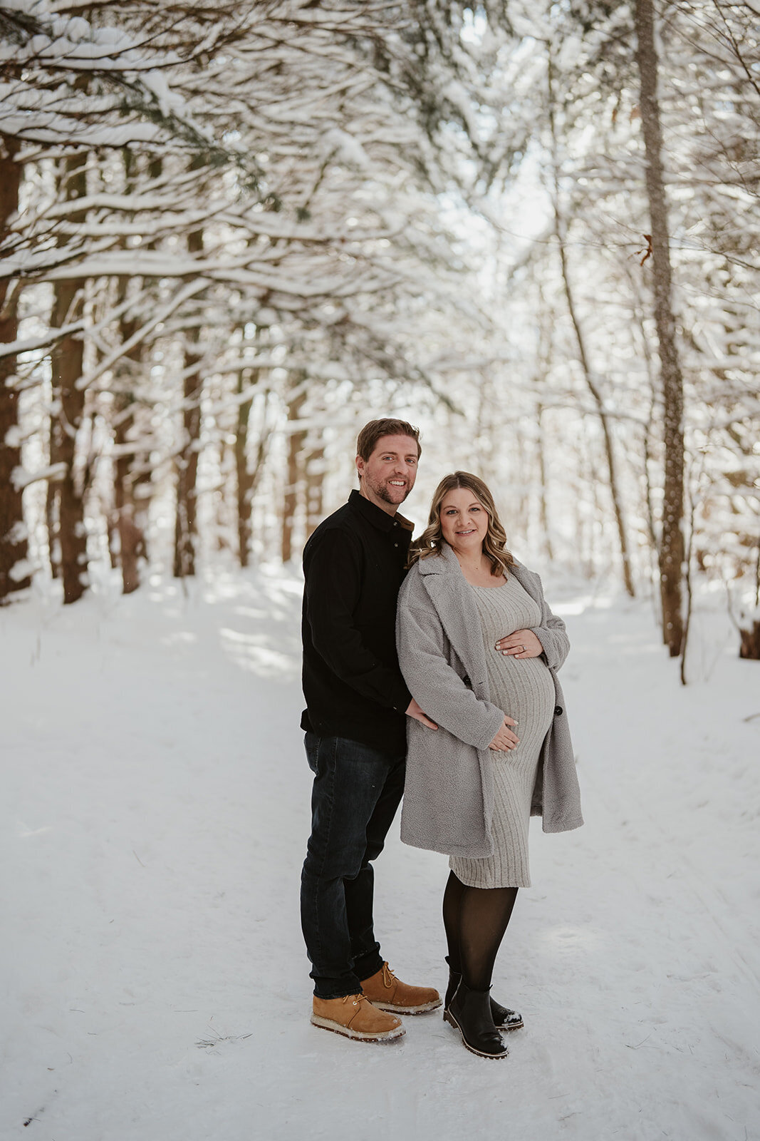 Expecting couple embracing in the snowy forest at Al Sabo Preserve during a Kalamazoo winter maternity photoshoot.