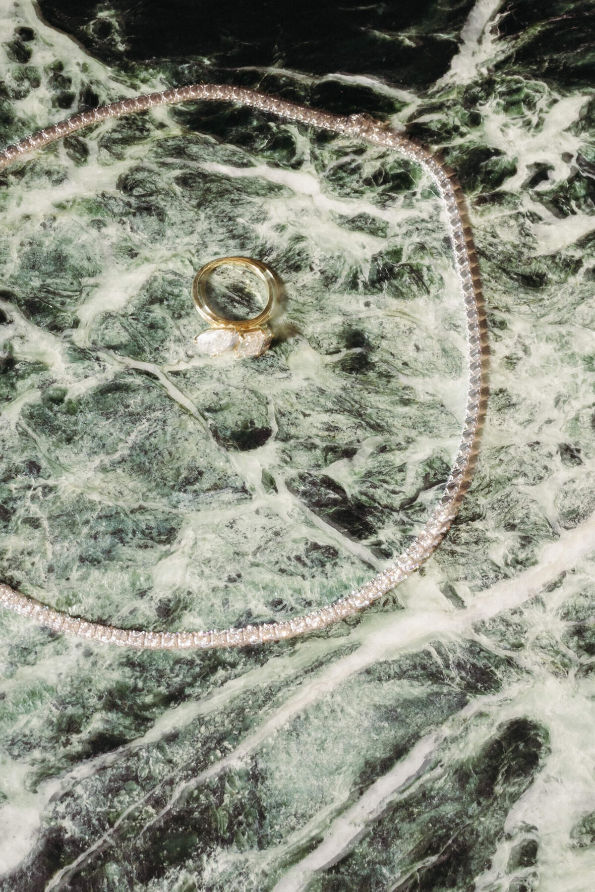 Close-up of wedding ring and necklace on marble surface before ceremony
