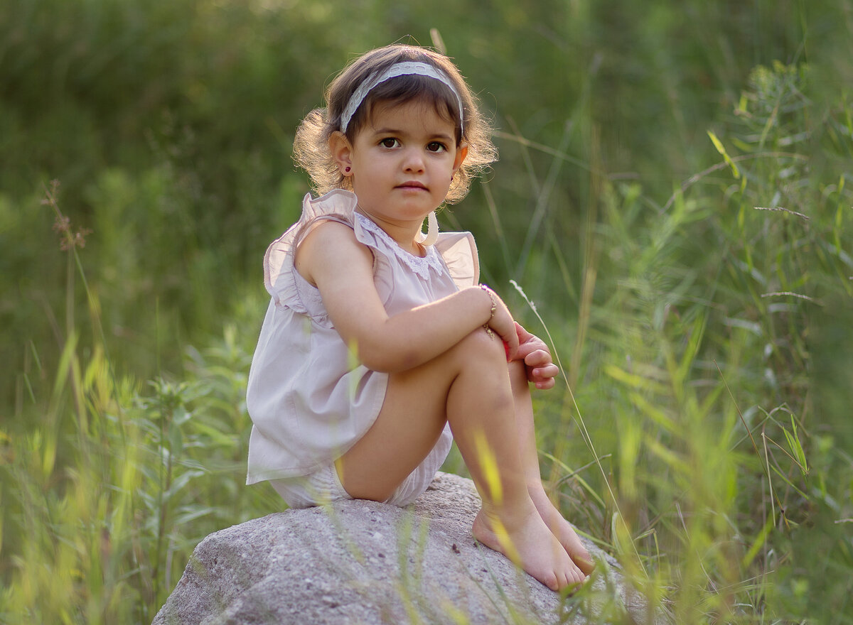 Little girl sits atop of a rock for a brooklyn, ny family photoshoot. Captured by premier Brooklyn NY family photographer Chaya Bornstein Photography.