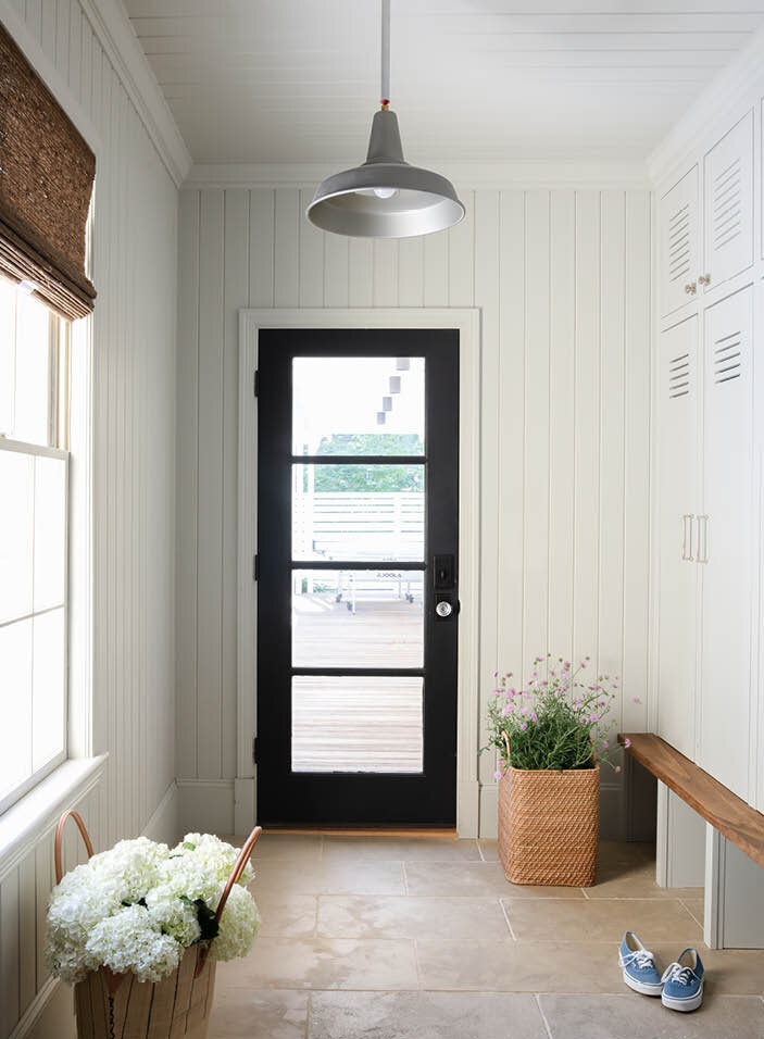 Discover the stylish mudroom in a historic Hingham home, featuring new doors, custom built-ins with shiplap walls, limestone flooring, and a walnut bench, coordinating with the adjacent laundry and powder room.