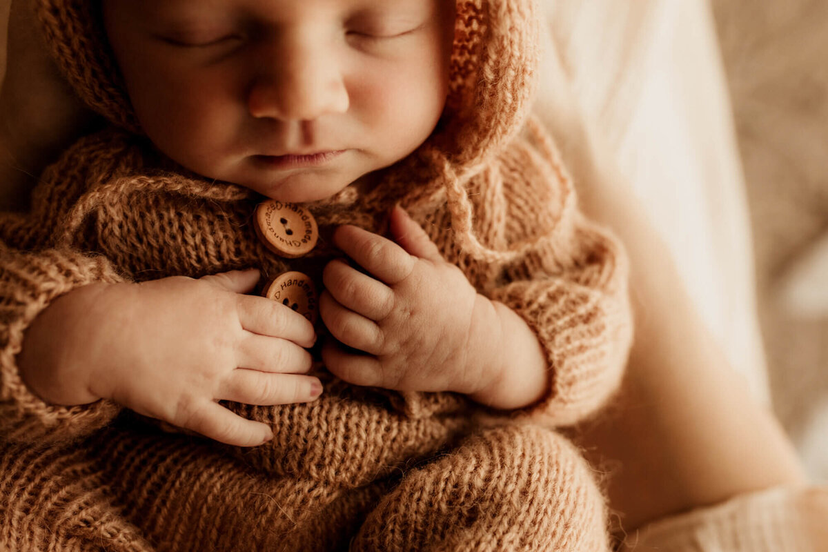 Baby boy sleeps on his mother's lap while wearing a hooded romper with buttons.
