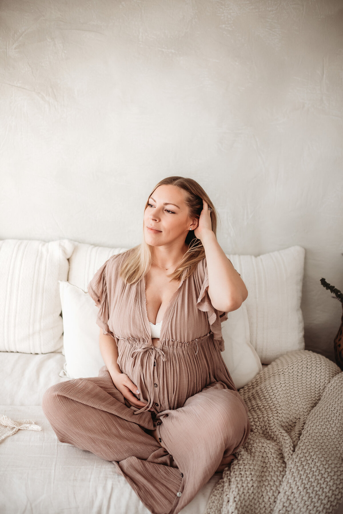 pregnant woman sitting crossed legged on bed putting her hand through her hair