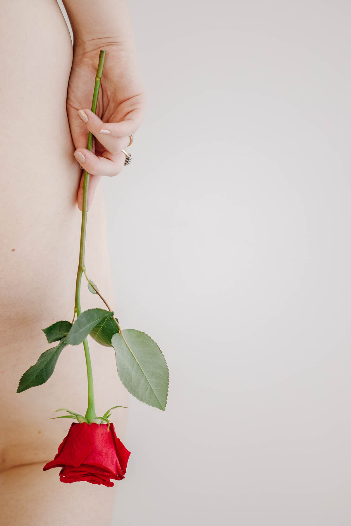 woman holds red rose on her leg during boudoir session