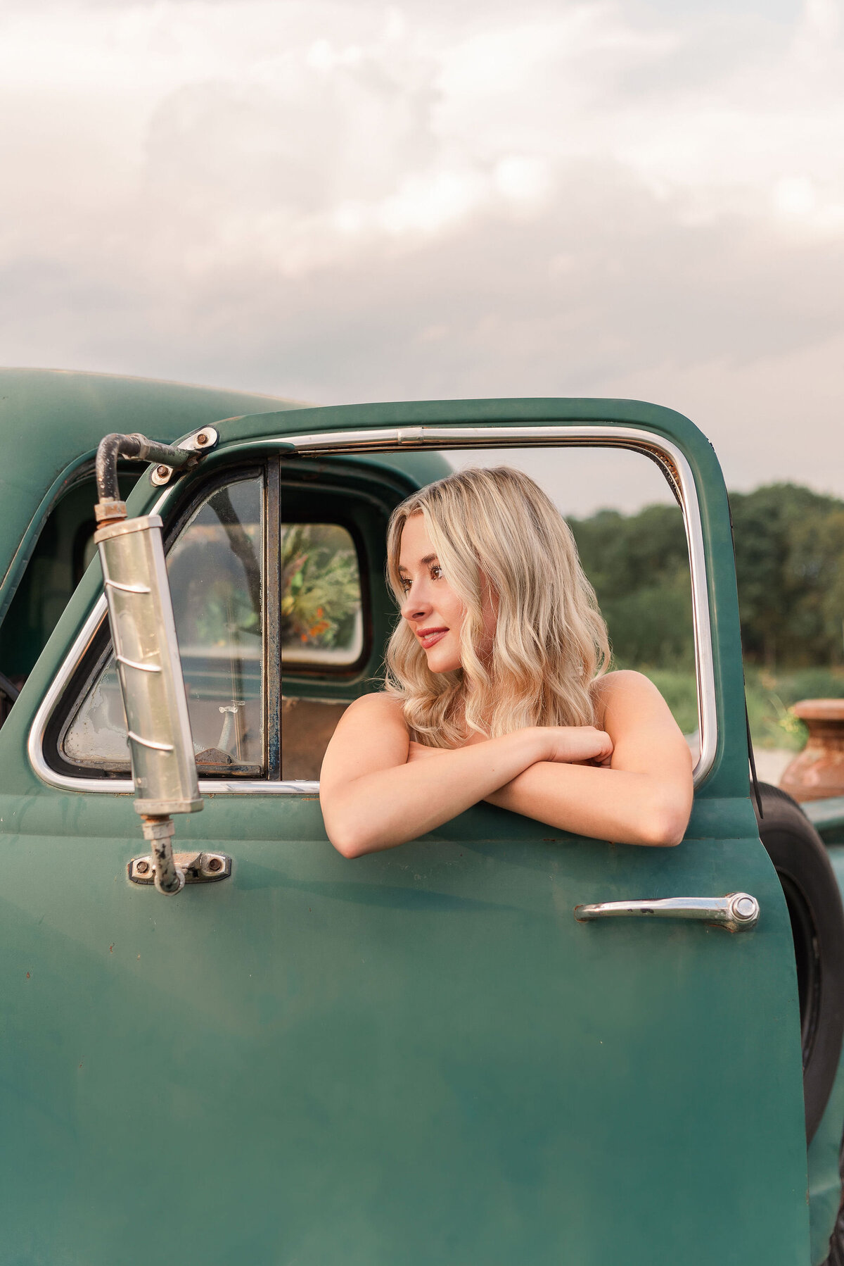 High school senior leaning out the window of a vintage green truck during golden hour — rustic senior photo session by Pittsburgh photographer Lens Love Photography.