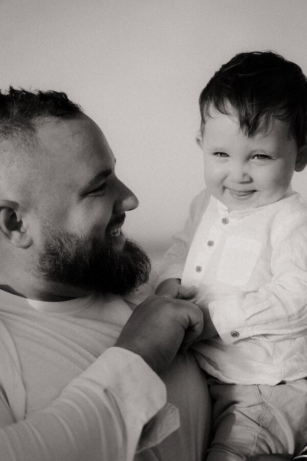 Complicité entre un père et son fils, regard tendre et éclats de rire. Photographie en noir et blanc par Kamescop.