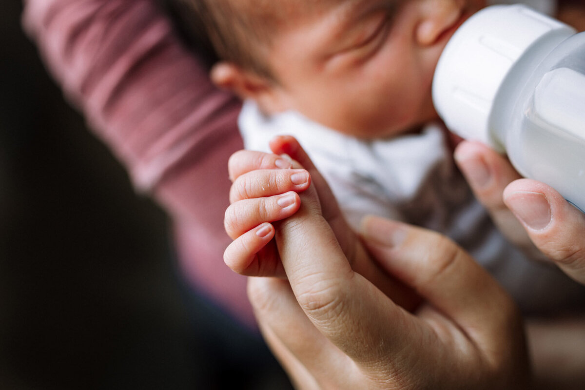 newborn fingers wrapped around mom's finger as she feeds baby a bottle