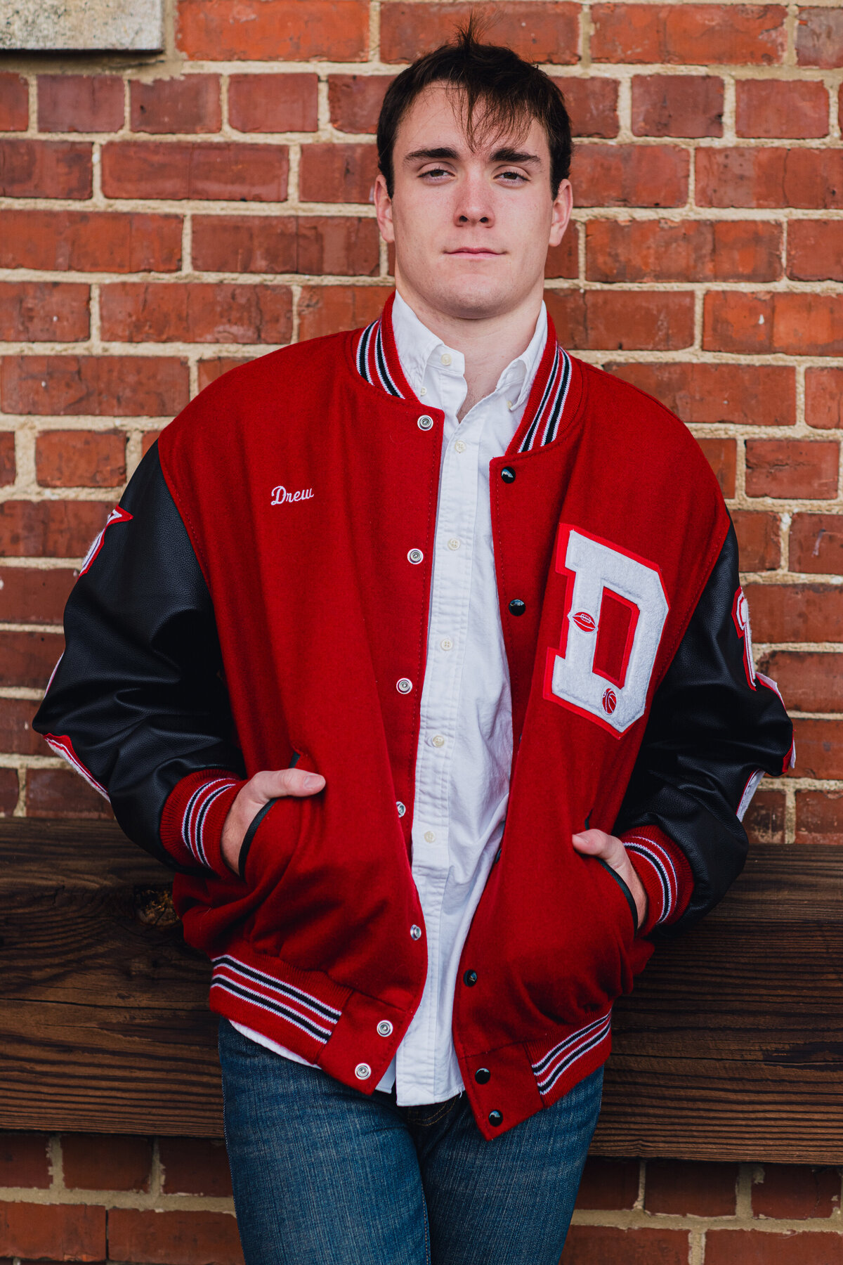 a basketball player in his lettermans jacket poses during his senior photo session in dalton