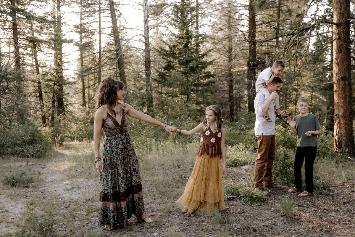 mom and daughter dancing in an open wooded area while dad and his sons are in the distance 