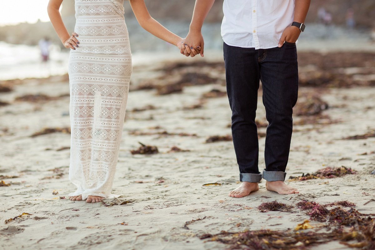 Engaged couple hold hands as they walk across the sandy beach
